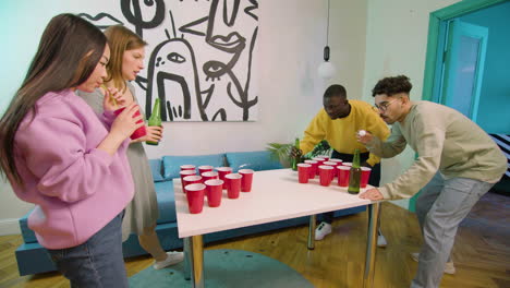 Happy-multiethnic-young-friends-playing-beer-pong-at-home