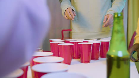 Close-up-of-unrecognizable-friends-playing-beer-pong-at-home