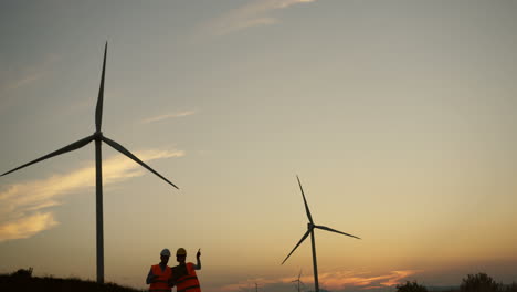 Two-male-and-female-engineers-talking-and-working-at-the-huge-windmills-turbines-at-the-sunset