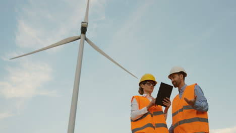 Lower-view-of-two-Caucasian-male-and-female-engineers-discussing-some-problems-and-reading-a-documento-at-the-wind-station-of-renewable-energy
