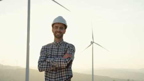 Caucasian-engineer-with-helmet-standing-at-the-huge-wind-turbine-station-and-looking-at-the-horizon
