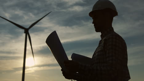Silhouettes-of-a-caucasian-woman-and-man-engineers-wearing-a-helmet-and-reading-some-documents-or-blueprints-at-wind-station-of-renewable-energy
