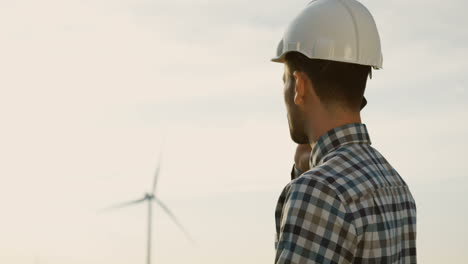 Side-view-of-Caucasian-man-engineer-wearing-a-helmet-talking-on-the-phone-at-wind-station-of-renewable-energy