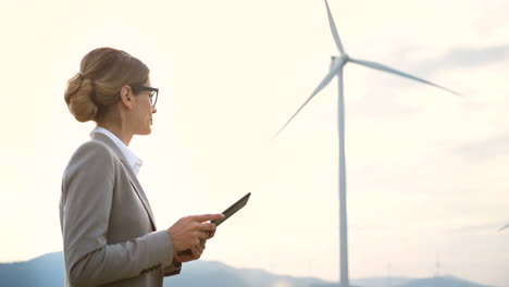 Side-view-of-caucasian-woman-engineer-using-a-tablet-at-wind-station-of-renewable-energy
