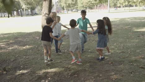 Happy-kids-holding-hands,-round-dancing-and-playing-playing-ring-a-ring-o'-roses-in-the-park