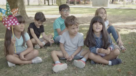 Niños-Multiétnicos-Sentados-Juntos-En-El-Césped-En-El-Parque-De-La-Ciudad