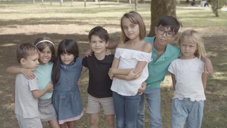 Multiethnic-children-standing-together-in-the-park,-hugging-and-smiling-at-the-camera