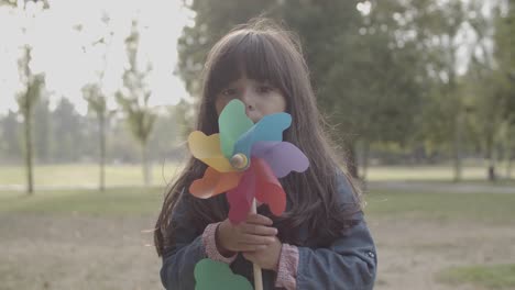Cute-Latin-girl-playing-with-paper-fan-and-blowing-on-it-in-the-park