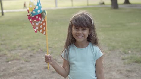 Lateinisches-Mädchen,-Das-Papierfächer-Hält,-Im-Park-Steht-Und-In-Die-Kamera-Lächelt