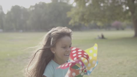 Latin-girl-holding-paper-fan,-running-and-smiling-in-the-park