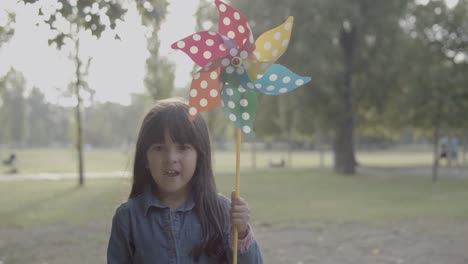 Latin-girl-holding-paper-fan,-standing-in-the-park-and-smiling-at-the-camera