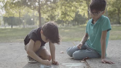 Two-cute-boys-sitting-on-ground-and-drawing-with-chalks