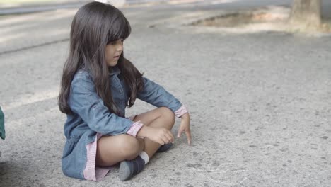 Brunette-girl-sitting-on-asphalt-and-drawing-with-chalks