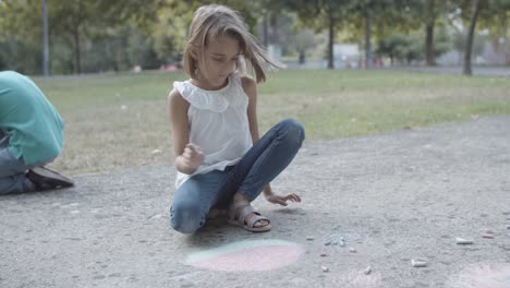 Blonde-girl-sitting-on-asphalt-and-drawing-with-chalk