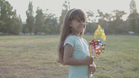 Adorable-little-girl-holding-a-paper-fan-at-the-park-and-looking-around