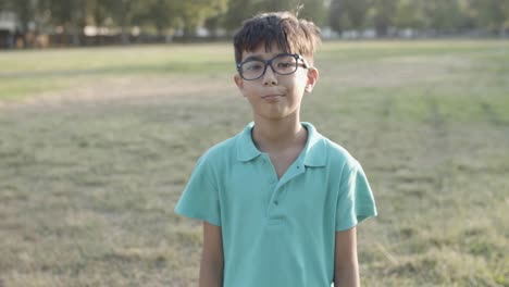 Portrait-of-cute-Latin-boy-standing-in-park-and-smiling-at-the-camera