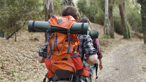 Couple-of-hikers-with-camping-backpacks-walking-on-forest-path