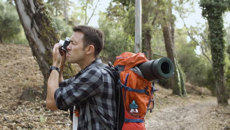 Active-tourist-guy-with-photo-camera-taking-pictures-of-forest