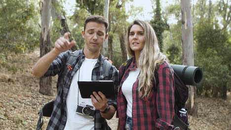 Couple-of-young-backpackers-using-tablet-in-forest