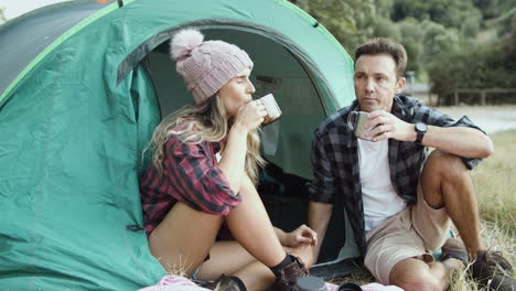 Camping-couple-eating-snacks,-drinking-hot-tea-or-coffee