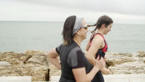 Triatletas-Femeninas-Enfocadas-Corriendo-A-Lo-Largo-Del-Paseo-Marítimo
