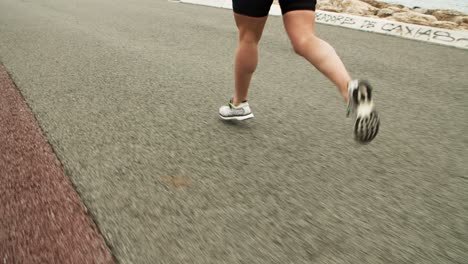 Legs-of-female-athlete-jogging-along-seaside-road
