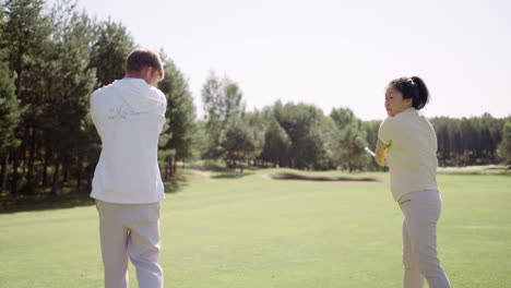Blond-trainer-teaching-asian-woman-how-to-play-golf