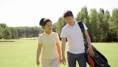 Asian-woman-and-man-talking-and-walking-on-golf-field