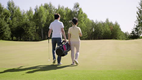 Back-view-of-couple-walking-and-holding-golf-clubs
