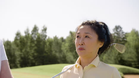 Mujer-Asiática-Hablando-Con-Su-Marido-Con-Un-Palo-De-Golf-En-El-Hombro