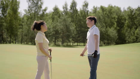 Asian-couple-holding-golf-clubs-and-talking-on-field