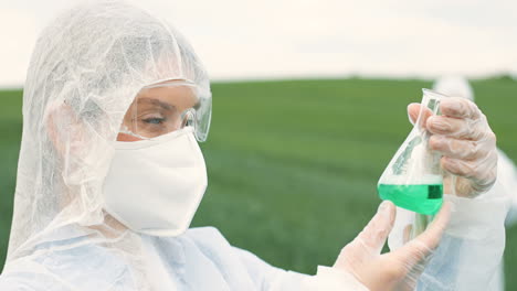Close-up-view-of-caucasian-researcher-woman-in-protective-suit-holding-test-tube-while-doing-pest-control-in-the-green-field