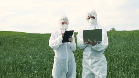 Caucasian-researchers-in-protective-suit-using-tablet-and-laptop-while-doing-pest-control-in-the-green-field