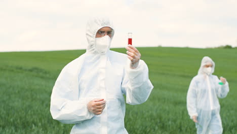 Caucasian-researcher-man-in-protective-suit-holding-test-tube-while-doing-pest-control-in-the-green-field