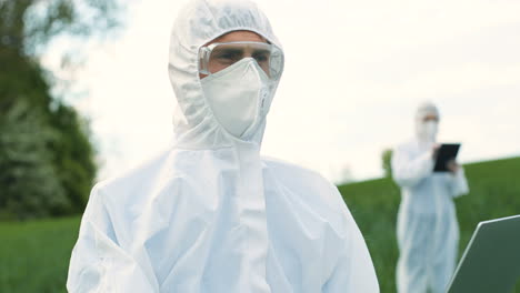 Close-up-view-of-caucasian-researcher-man-in-protective-suit-using-laptop-while-doing-pest-control-in-the-green-field