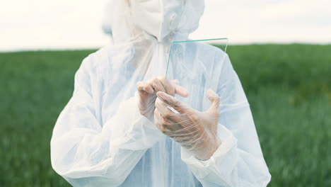 Rear-view-of-researcher-woman-hands-in-gloves-tapping-on-glass-in-the-green-field