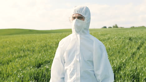 Caucasian-researcher-man-in-white-protective-suit-and-goggles-doing-pest-control-in-the-green-field