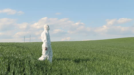 Side-view-of-caucasian-researcher-man-in-white-protective-suit-and-goggles-walking-in-the-green-field-while-doing-pest-control