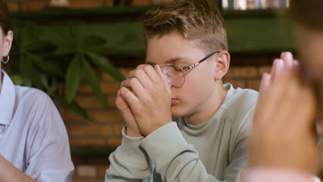 Blond-teenager-praying-next-to-his-teachers-and-classmates