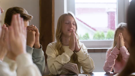 Young-girl-and-her-classmates-praying-in-religion-class