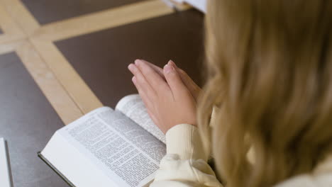Blond-girl-praying-with-her-hands-on-the-Bible-at-class