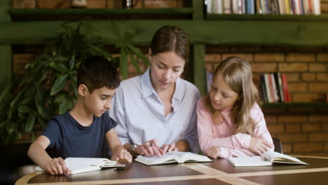 Brünette-Lehrerin-Liest-Mit-Zwei-Kleinen-Schülern-Die-Bibel