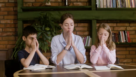 Two-pupils-praying-in-class-with-their-teacher