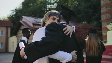 Graduado-Masculino-Abrazándose-Con-Su-Padre,-Papá-Felicitando-A-Su-Hijo-Con-Una-Graduación-De-La-Universidad