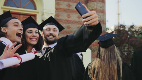 Foto-De-Retrato-De-Los-Graduados-Felices-Haciendo-Selfies-Con-Un-Teléfono-Inteligente-Cerca-Del-Edificio-De-La-Universidad