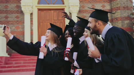 Grupo-De-Graduados-Multiétnicos-Haciendo-Selfies-Con-Un-Smartphone-Con-Sus-Diplomas-Cerca-De-La-Universidad