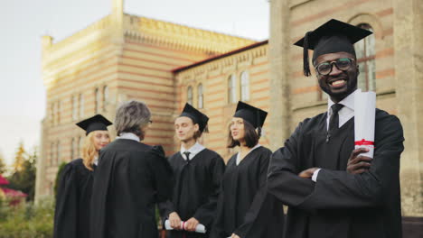 Portrait-of-an-African-American-smiled-male-graduate-posing-to-the-camera-and-crossing-his-hands-in-front-of-the-University