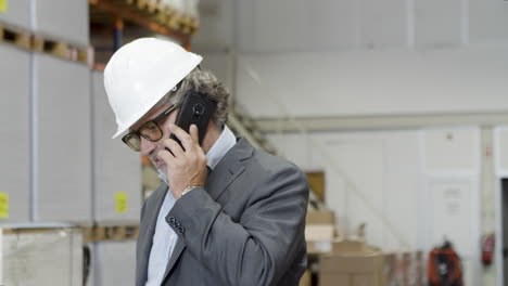 Focused-supervisor-in-eyeglasses-and-helmet-talking-on-phone-in-factory