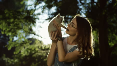 Young-caucasian-woman-in-glasses-holding-little-kitty-cat-and-petting-it-in-the-park-on-a-summer-day