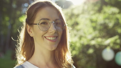 Close-up-view-of-a-Caucasian-woman-in-glasses-looking-and-smiling-at-camera-in-the-park-on-a-summer-day